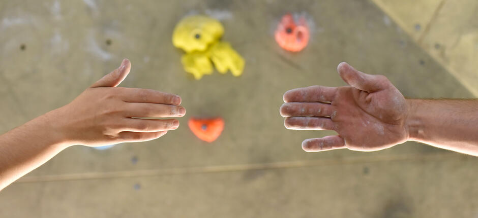 Zwei Menschen reichen sich die Hand vor Kletterwand Zwei Menschen reichen sich die Hand vor Kletterwand