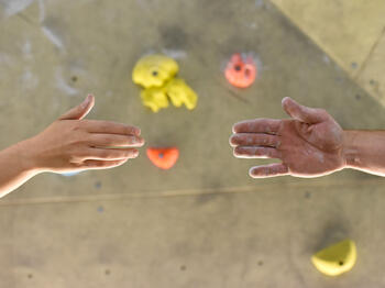 Zwei Menschen reichen sich die Hand vor Kletterwand Zwei Menschen reichen sich die Hand vor Kletterwand